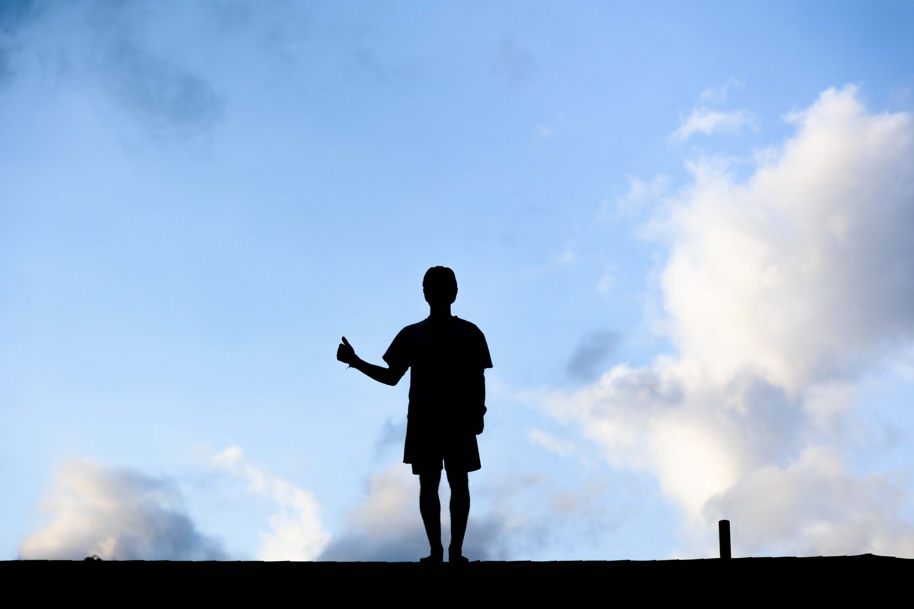 A silhouetted figure giving a thumbs up on a rooftop against a cloudy sky